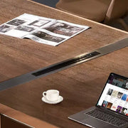 A sleek silver laptop with black keyboard on a luxury modern wooden conference room table with leather details