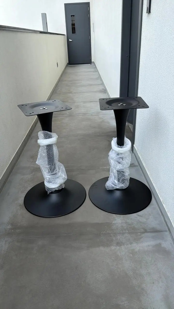 Black metal tulip legs with circular bases and conical stems wrapped in clear plastic for modern luxury table base