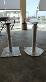 Load image into Gallery viewer, Two metallic stainless steel round column table legs wrapped in protective plastic standing on concrete floor